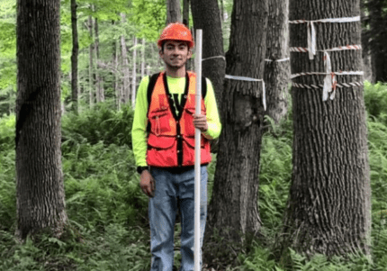 Brandon Marcucci '21 stands among trees in the Allegheny National Forest with gear to measure tree plots.